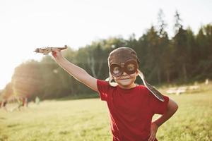 Niño feliz en casco de piloto jugando con un avión de juguete de madera y soñando con volar