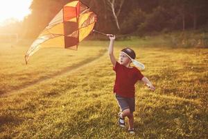 niño feliz lanza una cometa en el campo al atardecer. niño y niña en vacaciones de verano foto