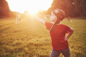 Happy kid in pilot helmet playing with a wooden toy airplane and dreaming of becoming flying photo