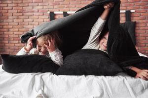 niños pequeños, niño y niña acostados y jugando con almohadas en la manta de la cama con una manta