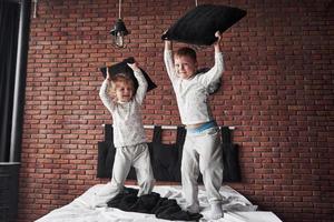 Naughty children Little boy and girl staged a pillow fight on the bed in the bedroom. They like that kind of game photo