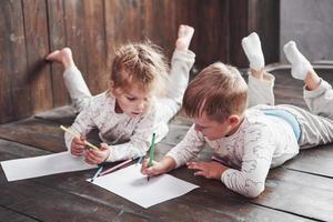 los niños se acuestan en el suelo en pijama y dibujan con lápices. lindo niño pintando con lápices foto