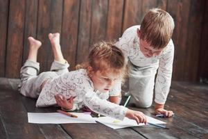 Children lie on the floor in pajamas and draw with pencils. Cute child painting by pencils photo