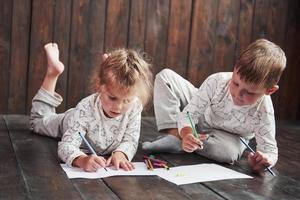 los niños se acuestan en el suelo en pijama y dibujan con lápices. lindo niño pintando con lápices