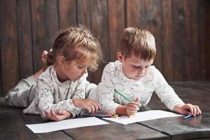 los niños se acuestan en el suelo en pijama y dibujan con lápices. lindo niño pintando con lápices foto