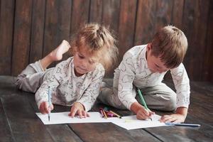 Children lie on the floor in pajamas and draw with pencils. Cute child painting by pencils photo