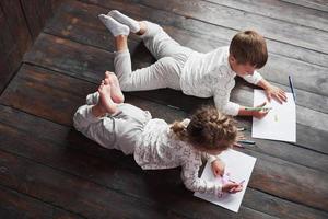 Children lie on the floor in pajamas and draw with pencils. Cute child painting by pencils photo