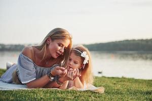 Attractive happy young mother lying with her cute daughter on the grass in the park. photo