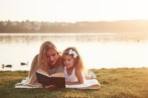 madre con un niño lee un libro en la hierba foto