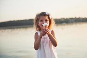 una hermosa niña come un helado cerca del agua