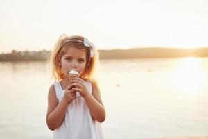 A beautiful little girl eats an ice cream near the water photo