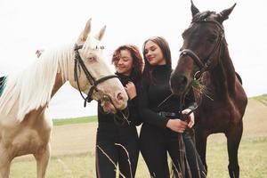 dos hermosas chicas jóvenes en marcha para montar cerca de sus caballos. ellos aman a los animales foto