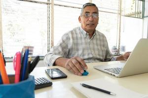 Mature man looking at camera sitting in front of laptop computer. photo