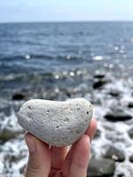 Piedra en forma de corazón en la mano de las niñas contra el fondo de la playa. día soleado de verano. concepto de amor, boda y día de San Valentín. encontrando piedras hermosas e interesantes. vacaciones en la playa