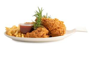 Pollo frito y papas fritas con hoja de romero, comida chatarra alta en calorías servida en un plato blanco aislado sobre fondo blanco con trazado de recorte foto