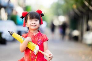 Beautiful Asian girl holding umbrella with closed, yellow vintage style. Children smile sweet and happy. Child wore a red Chinese New Year dress and a furry red hair clip. Adorable kid 3-4 years old. photo