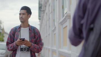 Hombre asiático con un teléfono inteligente comprobando el mapa mientras está de pie junto a la calle en Tailandia. video