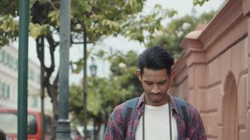 Asian man using a smartphone checking social media while walking beside the street in Thailand. video