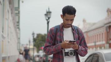 Hombre asiático que usa un teléfono inteligente para comprobar el mapa mientras está de pie junto a la calle en Tailandia. video