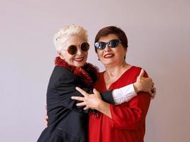 dos hermosas mujeres mayores maduras con estilo en gafas de sol abrazándose. diversión, fiesta, estilo, concepto de celebración foto