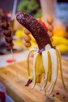 Banana on a stick coated chocolate with coconut chips and colored candies photo