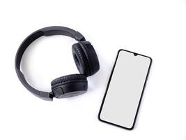 Auriculares inalámbricos negros y teléfonos inteligentes móviles con una maqueta de pantalla en blanco sobre la superficie de un fondo blanco