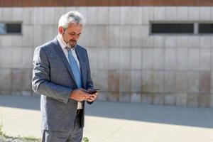 Senior businessman texting with smartphone outside of modern office building. photo