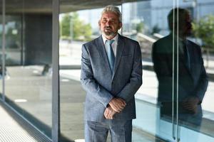 hombre de negocios senior con los brazos cruzados fuera del moderno edificio de oficinas. foto