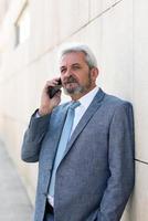 Senior businessman with smartphone outside of modern office building. photo