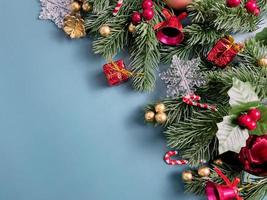adornos navideños, hojas de pino, bolas doradas, copos de nieve, frutos rojos y frutos dorados sobre fondo azul foto
