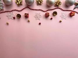 Christmas decorations, gift box ribbons, golden balls, snowflakes, red balls on pink background photo