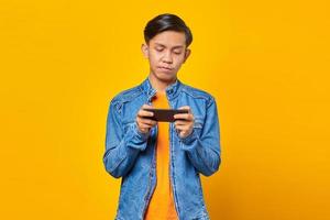 asian man using mobile phone playing game with angry face over yellow background photo