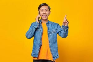 Shocked Asian youth while talking on the smartphone and finger pointing up. yellow background photo