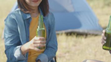 mujer asiática feliz con amigos acampando en la naturaleza divirtiéndose juntos bebiendo cerveza y tintineando vasos. video