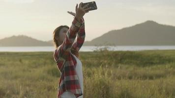 chat video selfie donna asiatica con i suoi amici sullo smartphone durante il tramonto.