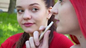 Deux belles filles fumant une cigarette électronique iqos dans un parc d'été