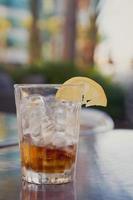 Glass with cola, ice and lemon on a table outside photo