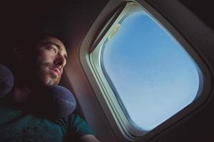 Pensive man with neck pillow looking outside through the window of an airplane photo