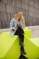 Mujer joven escuchar música desde un teléfono móvil en un banco público moderno foto