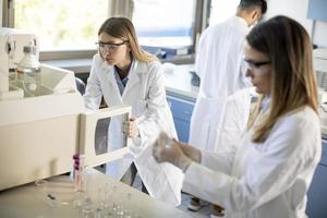 Mujeres científicas en una bata de laboratorio blanca poniendo un frasco con una muestra para un análisis en un sistema de ioncromatografía en un laboratorio biomédico foto