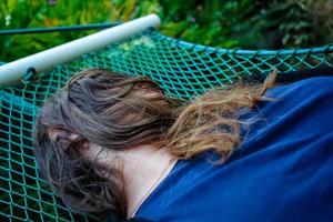 Woman laying down on a hammock and her face covered by her hairs photo