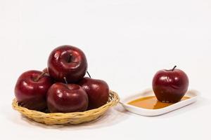 Montón de manzanas rojas y manzana roja en un plato blanco con miel aislado sobre un fondo blanco.