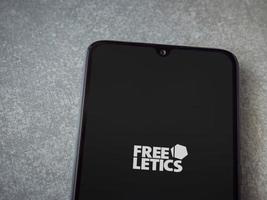 Freeletics Training Coach app launch screen with logo on the display of a black mobile smartphone on ceramic stone background