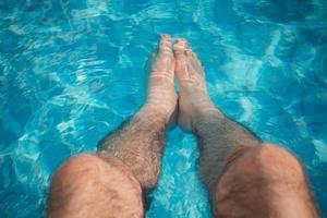 Relajación joven en la piscina con las piernas en el agua foto