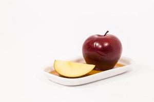 Rodaja de manzana roja y manzana roja sobre un plato blanco con miel aislado sobre un fondo blanco. foto