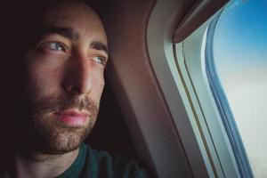 Cerca de un hombre pensativo mirando hacia afuera a través de la ventana de un avión foto