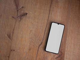 Black mobile smartphone mockup lies on the surface with blank screen isolated on wooden background photo