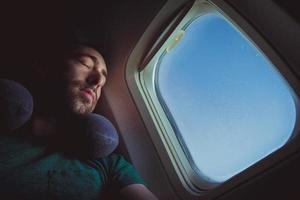 Hombre joven con almohada para el cuello descansando y durmiendo en un avión foto