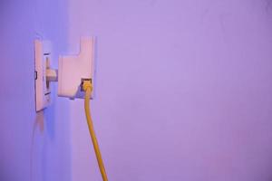 WiFi extender in electrical socket on the wall with ethernet cable plugged in photo