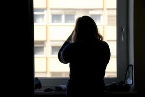 Back view of silhouette of a woman putting on makeup in front of a window photo
